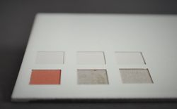 Gezeigt wird die laserbasierte, stufenweise Abtragung der Beschichtung eines lackierten Bleches (von links nach rechts & oben nach unten), wobei die haftungsvermittelnde Grundierung rötlich gefärbt ist.