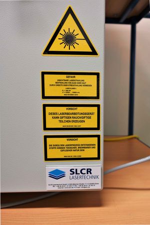 The picture shows a part of the control box of the CO2-laser workstation. There are many signs with warnings. 