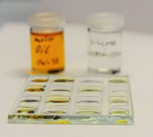 The picture shows a chessboard-like oleophobically structured glass substrate on which motor oil and silicone oil have been alternately applied and rectangular drops of oil form.