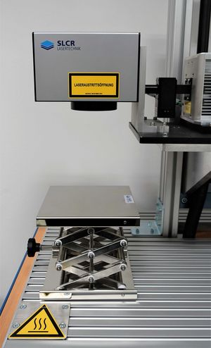 Die Abbildung zeigt den Scannerkopf und den Probenhubtisch des CO2-Laser Arbeitsplatzes.
