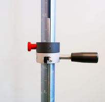Ball impact tester: A detailed view of the release mechanism is shown. The picture shows a vertical, long, slotted tube. Inside the tube is a drop weight with a mandrel pointing forward through the slot. This mandrel is mounted in a holding device. By turning the holding device, the mandrel is mechanically released and the weight can fall down.