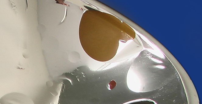 Die Abbildung zeigt einen Schadensfall an einem Lichtreflektor, dessen Beschichtung Abplatzungen und Blasen aufweist.