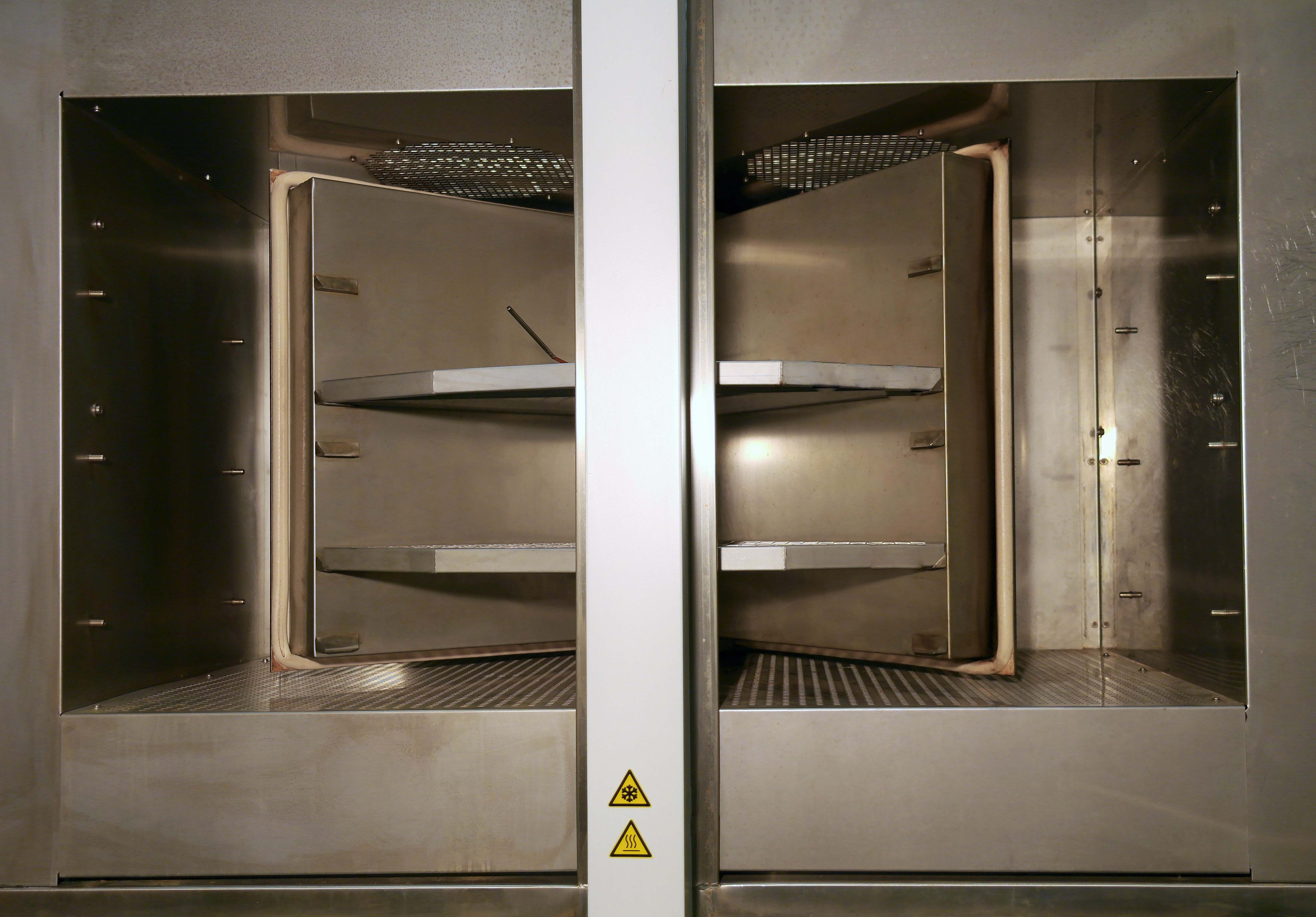 Die Abbildung zeigt eine Temperaturschockkammer TSK 200. Beide Kammern sind geöffnet. Der Fahrkorb befindet sich zwischen beiden Kammern in Mittelstellung. Im Fahrkorb sind zwei Blecheeinsätze montiert.
